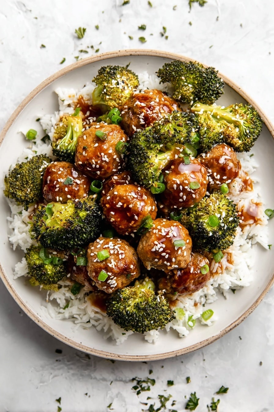 A white plate filled with three layers: the bottom layer is white fluffy rice, the middle layer is round meatballs coated in a shiny brown sauce, and the top layer is bright green broccoli florets with a slightly charred texture. The meatballs and broccoli are sprinkled with white sesame seeds and small pieces of chopped green herbs. The plate is on a white marbled surface with small bits of herbs scattered around. photo taken with an iphone --ar 2:3 --v 7 - Freezer Teriyaki Chicken Meatballs, Teriyaki Chicken Meatballs, Make-Ahead Dinner, Healthy Meal Prep, Freezer-Friendly Meatball Recipe