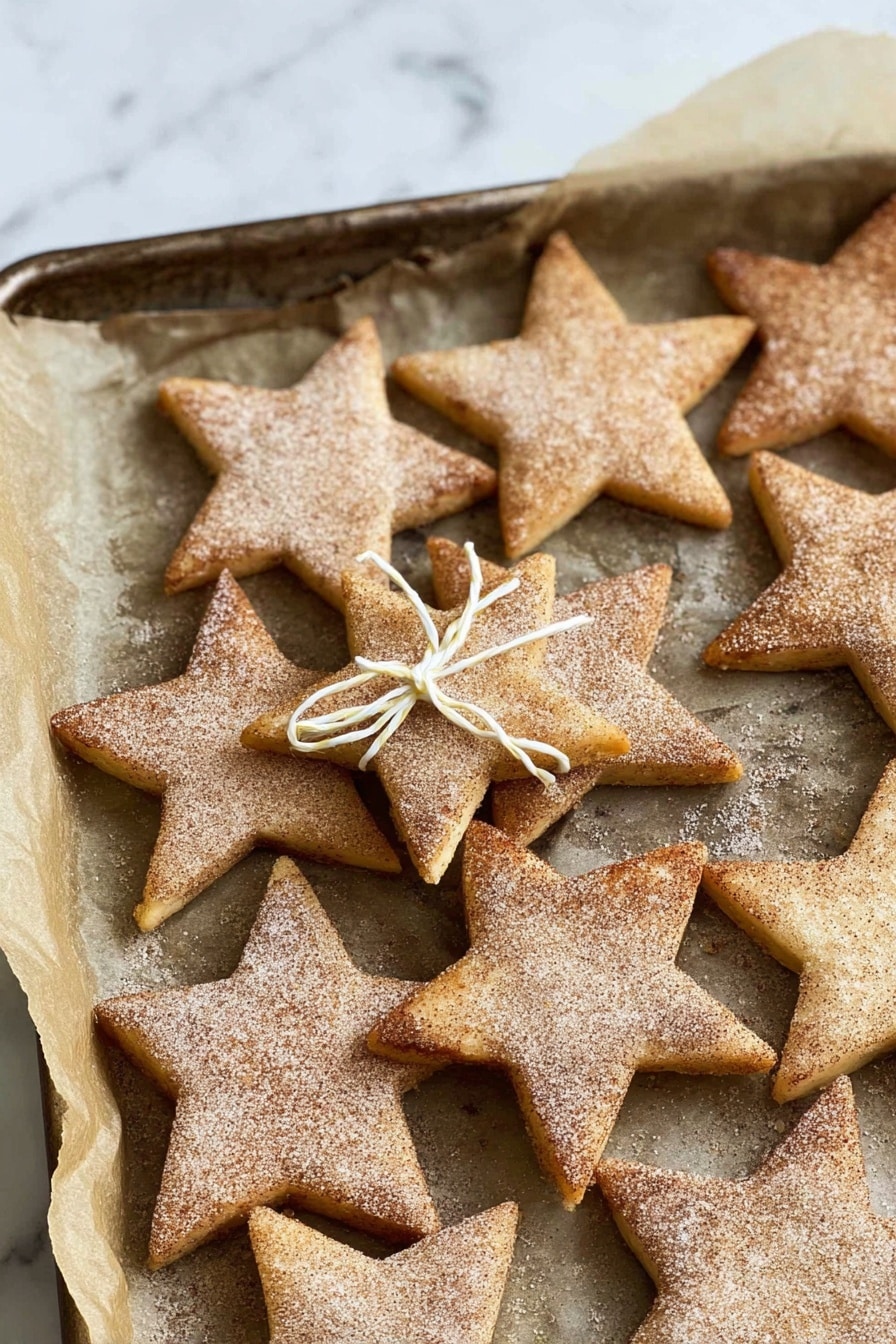 The image shows four star-shaped cookies placed on a white marbled textured surface covered with white translucent paper, which rests on a silver cooling rack. Each cookie is golden brown with a slightly darker edge, and they have a rough texture with a visible dusting of cinnamon sugar on top, giving them a speckled look. The cookies are evenly spaced, and in the bottom left corner, two cinnamon sticks are placed parallel to each other. To the right, there is a piece of yellow and white string tied into a small bow. Photo taken with an iphone --ar 2:3 --v 7 - Cinnamon Shortbread Cookies, Cinnamon Shortbread Cookies recipe, buttery shortbread cookies, easy cinnamon cookies, festive holiday cookies
