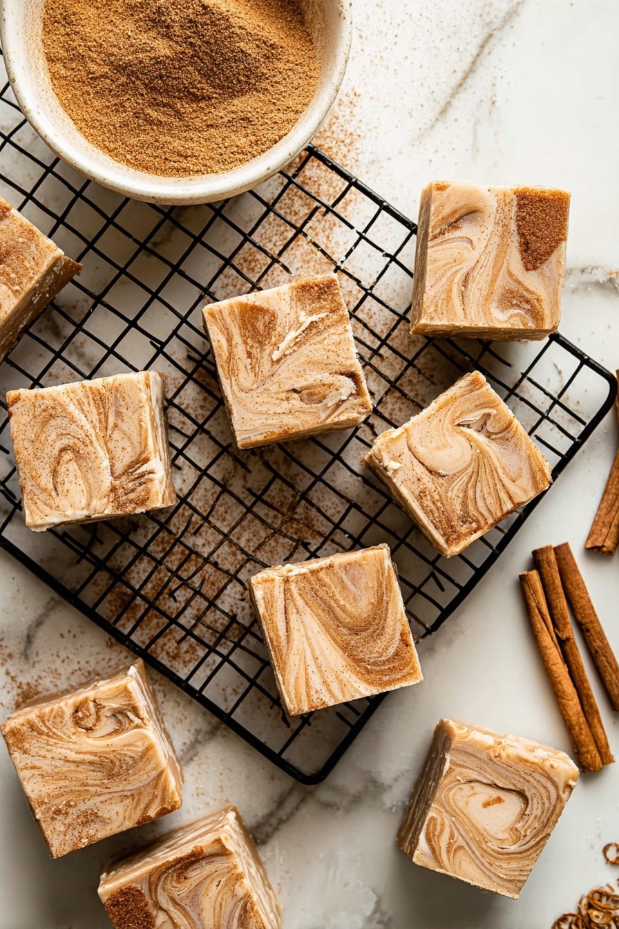The image shows square pieces of fudge with a two-layer look. The bottom layer is light cream color with a smooth texture, while the top layer is swirled with light and dark brown shades, creating a marbled effect dusted with cinnamon powder. The fudge pieces are placed on a black cooling rack on a white marbled surface. In the top left corner, there is a white bowl filled with cinnamon powder, and on the right side, some cinnamon sticks are partly visible. The fudge pieces are arranged casually, some slightly overlapping each other, and one piece shows the inside texture with a bite taken out. photo taken with an iphone --ar 2:3 --v 7 - Cinnamon Sugar White Chocolate Fudge, white chocolate fudge, cinnamon fudge recipe, easy holiday fudge, homemade fudge dessert
