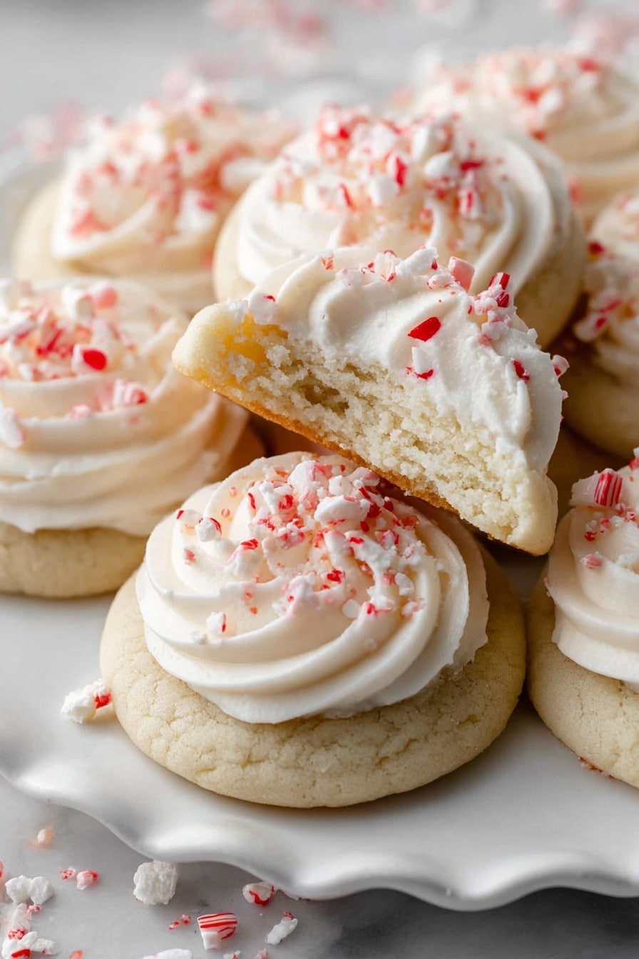 The image shows soft, thick cookies with a light beige color, each topped with a swirl of creamy white frosting. The frosting is smooth and piped in a circular, rose-like fashion on the center of each cookie. Small pieces of red and white candy, resembling crushed peppermint, are sprinkled on top of the frosting and scattered around the cookies. The cookies are arranged close together on a white marbled surface, filling the frame with a cozy and inviting look. photo taken with an iphone --ar 2:3 --v 7 - Peppermint Meltaways Cookies, holiday peppermint cookies, buttery peppermint cookies, peppermint dessert recipes, Christmas cookies