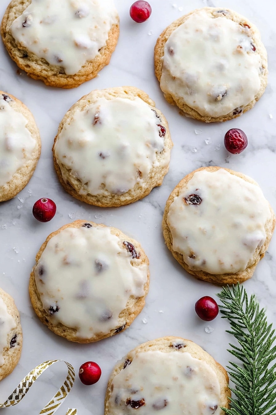A woman's hand holds two halves of a round cookie close to the camera, showing the inside texture. Each cookie has two layers: a light golden-brown base with small dark red cranberry bits inside, and a thin white icing layer on top. The icing looks smooth and slightly shiny, covering the entire top of the cookies. In the background, several whole cookies with the same two layers are spread out on a white marbled surface. The colors mainly are light brown, white, and dark red. photo taken with an iphone --ar 2:3 --v 7 - Lemon Cranberry Cookies, lemon cranberry cookie recipe, tart and sweet cookies, easy lemon cookie recipes, fruity holiday cookies