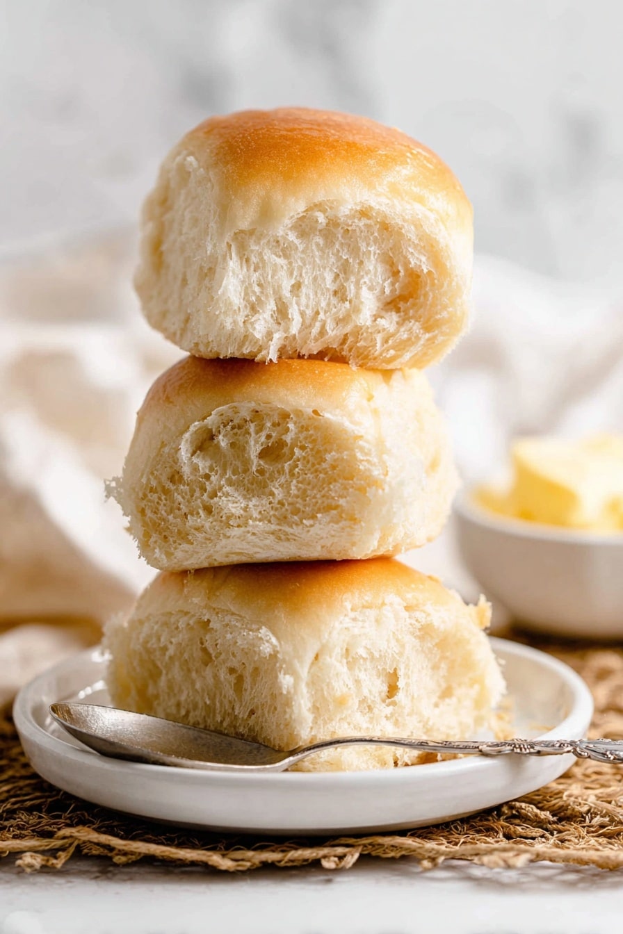 The image shows a close-up of a set of golden-brown dinner rolls arranged in a grid, with a total of 12 rolls visible, each one square-shaped with smooth, shiny tops that reflect light softly. The rolls have a rich, even bake with slightly darker edges and softer, lighter sides where they touch each other, creating a uniform pattern. The texture on top looks soft and fluffy, with a slight dome shape on each roll, and the bottoms are not visible. The background is a white marbled texture. photo taken with an iphone --ar 2:3 --v 7 - Soft Homemade Yeast Rolls, fluffy yeast roll recipe, buttery dinner rolls, easy yeast bread, homemade bread rolls