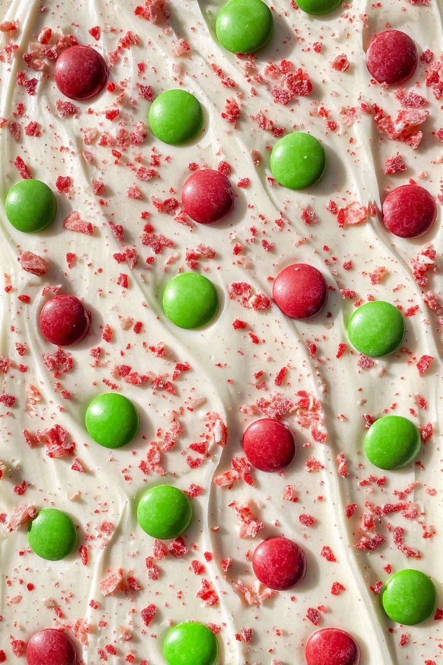 The image shows one thick white layer of creamy textured bark spread wide, sprinkled with small red crushed pieces all over. On top, there are evenly spread round candies in bright red and green colors, each smooth and shiny. The background is a white marbled surface that helps the bright colors stand out clearly. photo taken with an iphone --ar 2:3 --v 7 - Chocolate Peppermint Bark, Christmas chocolate treat, festive holiday dessert, easy peppermint candy bark, homemade holiday chocolates