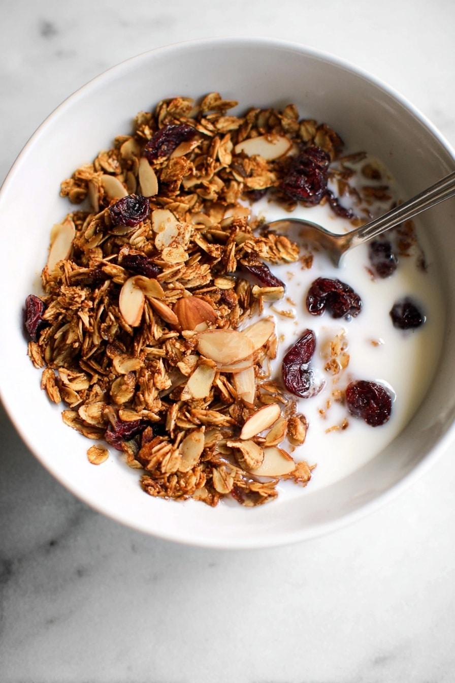 A white bowl filled with a mound of granola resting on a white marbled surface. The granola has a rough texture with visible clusters of toasted oats, nuts like pecans, and dried red berries mixed in. The colors are mainly golden brown with hints of deep red scattered throughout. The bowl is centered, filling the frame about halfway up, with a neutral soft background. Photo taken with an iphone --ar 2:3 --v 7 - Gingerbread Granola, gingerbread granola recipe, cozy breakfast ideas, holiday granola, spiced granola