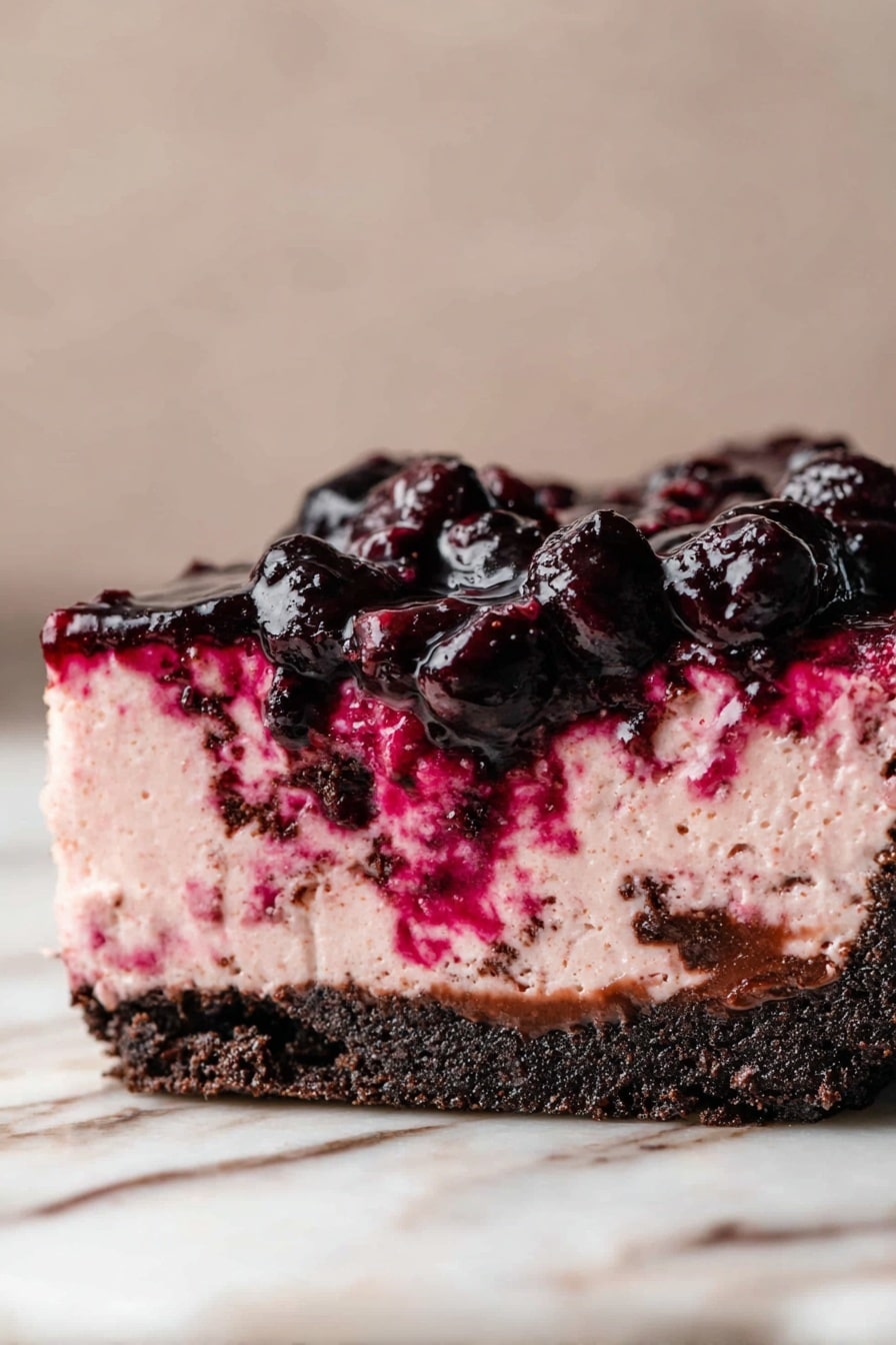 A slice of creamy pink berry mousse cake sits on a white plate with thin golden lines radiating out from the center. The cake has three visible layers: the top and middle are smooth light pink mousse with bits of berry mixed inside, and the bottom is a dark, crumbly chocolate crust. Dark berry sauce with whole berries drips down the side and pools on the plate, mingling with some mousse spread by a silver spoon resting on the edge. The background is a soft white marbled surface. Photo taken with an iphone --ar 2:3 --v 7 - Cherry Cheesecake with Oreo Crust, cherry cheesecake with oreo crust, best cherry cheesecake dessert, easy cherry cheesecake recipe, homemade cherry cheesecake