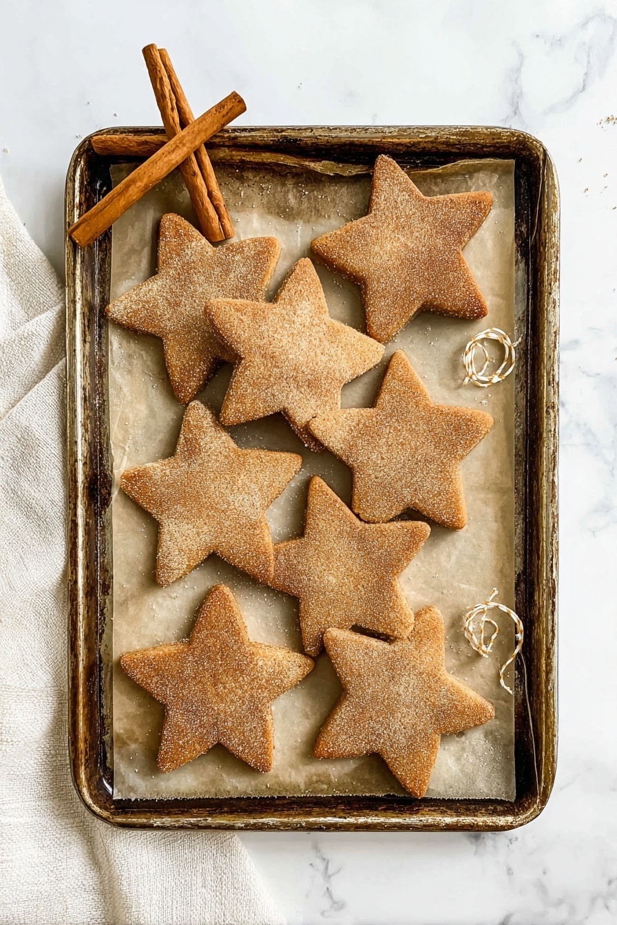 Seven star-shaped cookies with a light brown color and a sugar and cinnamon coating on top are arranged on an old metal baking tray lined with parchment paper. Two cinnamon sticks are placed at the top left of the tray, and a piece of thin white and yellow string lies softly on the right side near one cookie. The tray sits on a white marbled surface with a soft white towel partially visible along the left edge. The cookies have a slightly rough texture and a warm, baked look. photo taken with an iphone --ar 2:3 --v 7 - Cinnamon Shortbread Cookies, Cinnamon Shortbread Cookies recipe, buttery shortbread cookies, easy cinnamon cookies, festive holiday cookies