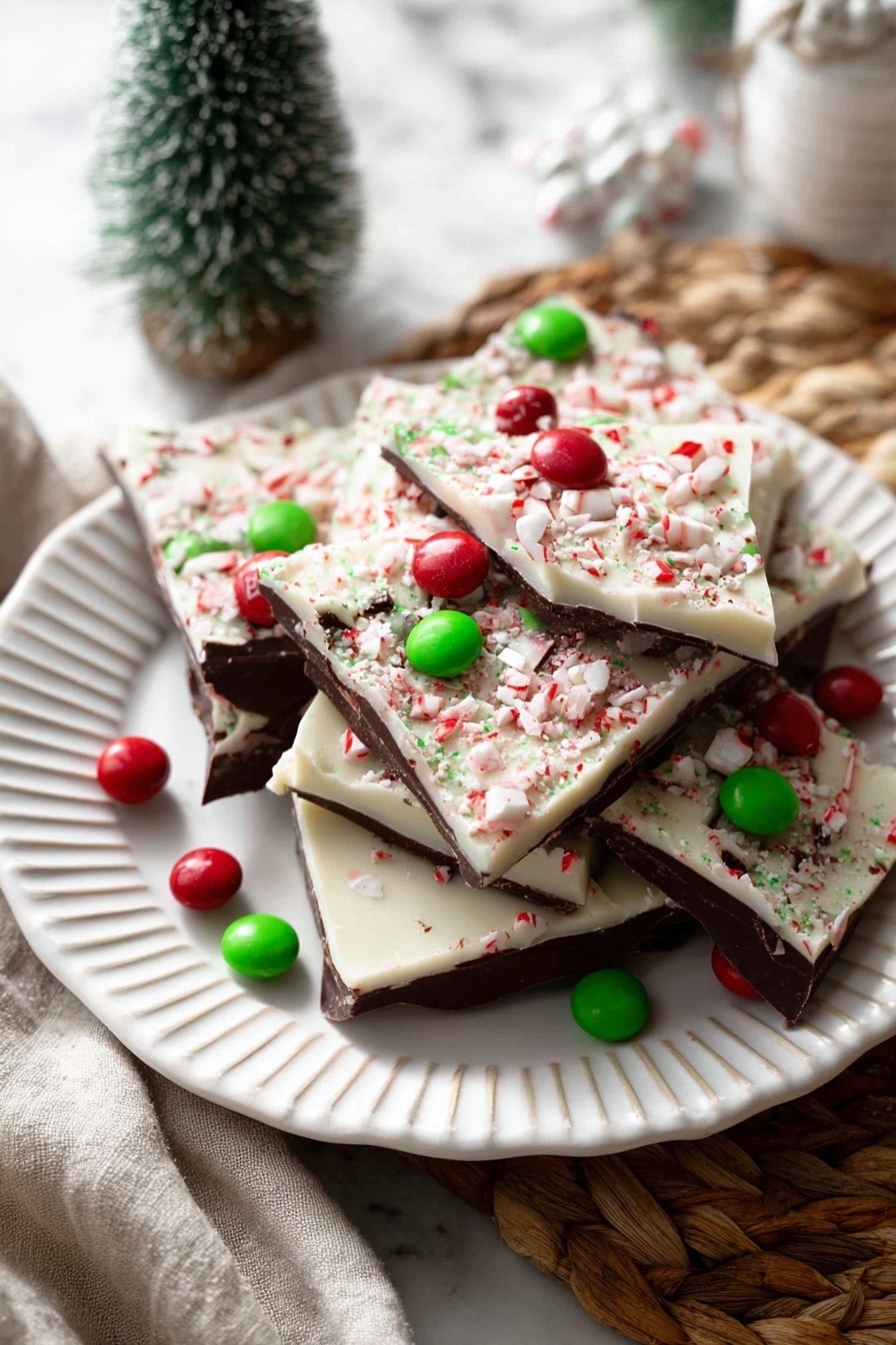 A stack of five large chocolate bark pieces sits on a round wooden slice on a white marbled surface. Each bark layer is mostly dark brown with a thick creamy white top layer sprinkled with crushed candy cane bits. Bright red and green candy-coated chocolates are scattered and pressed into the bark's white topping. One piece of bark leans on the stack to the right, showing its smooth white layer with a red candy on top. In the background, a small decorated green tree and red and white ornaments add a festive touch. photo taken with an iphone --ar 2:3 --v 7 - Chocolate Peppermint Bark, Christmas chocolate treat, festive holiday dessert, easy peppermint candy bark, homemade holiday chocolates