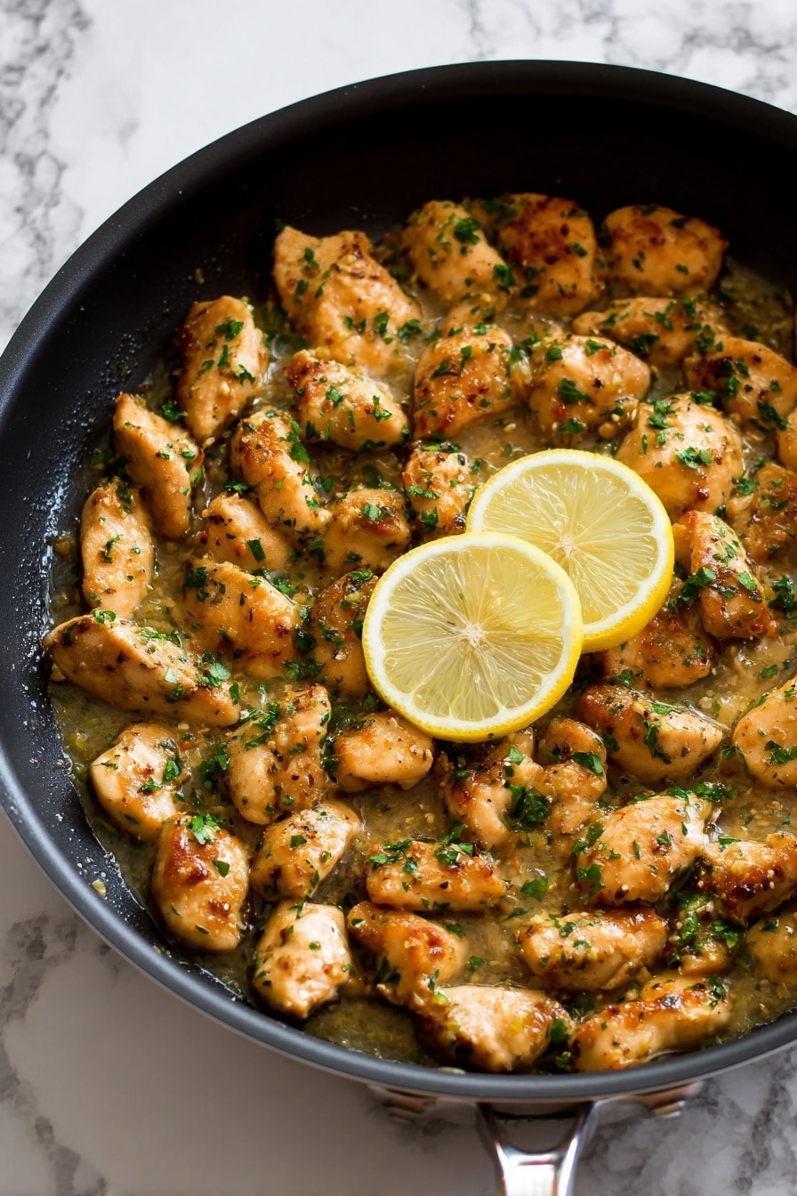 The image shows a black frying pan filled with many small, golden-brown chicken pieces cooked in a light sauce. The chicken pieces are sprinkled with chopped green herbs that add a fresh look. Among the chicken, there are two bright yellow lemon slices standing out. The sauce looks shiny and slightly thick, covering the pan’s base and partially surrounding the chicken. The pan is set on a white marbled surface, with its metal handle partially visible at the bottom. photo taken with an iphone --ar 2:3 --v 7 - Chicken Scampi with Wine and Lemon, easy chicken pasta with lemon and white wine, quick chicken scampi recipe, lemon chicken pasta dinner, flavorful chicken pasta dishes