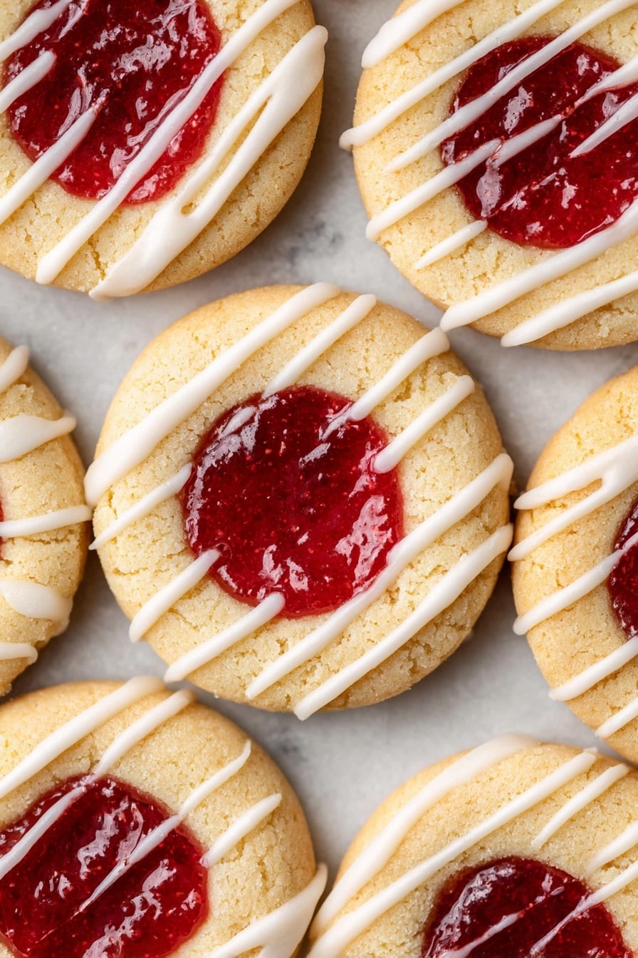 The image shows several round cookies with two layers: a light golden beige shortbread base and a bright red jam filling in the center. The jam looks smooth and shiny, sitting in a small circular well in the middle of each cookie. Each cookie is decorated with thin white icing stripes unevenly drizzled across the top. The cookies are placed close together on a white marbled textured surface, filling the frame almost completely. Photo taken with an iphone --ar 2:3 --v 7 - Jam Thumbprint Cookies, thumbprint cookie recipe, homemade jam cookies, buttery jam cookies, holiday cookie recipes