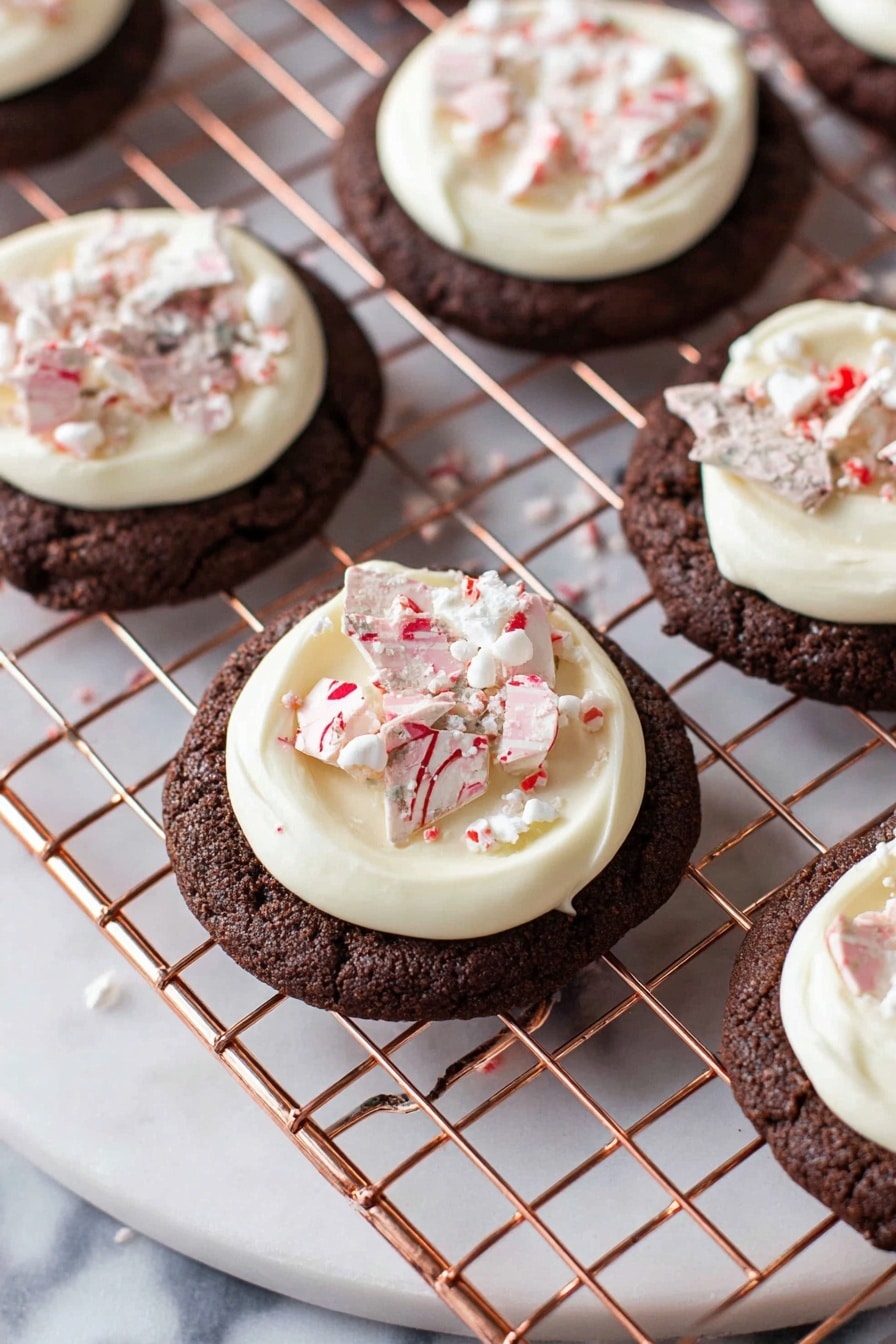 The image shows round chocolate cookies on a copper wire cooling rack over a white marbled surface. Each cookie has one thick, smooth layer of white cream frosting swirled on top. On the frosting, there are pieces of marbled white and pink candy shards sprinkled with tiny white and red crushed bits. The cookies have a slightly cracked texture around the edges. The scene is bright and clear, focusing closely on the cookies. photo taken with an iphone --ar 2:3 --v 7 - Peppermint Bark Cookies, peppermint bark cookies recipe, holiday chocolate peppermint cookies, peppermint cookie recipe, festive peppermint treats