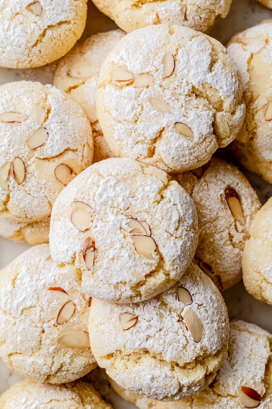 A stack of light golden almond cookies on a white marbled surface, with five cookies in total. The top four cookies are whole, with a rough, cracked texture and a dusting of powdered sugar. The bottom cookie in front has a bite taken out, showing a soft, moist inside with small chunks, and a few thin almond slices on top covered lightly with powdered sugar. The cookies are round and slightly puffy, arranged in a neat stack. photo taken with an iphone --ar 2:3 --v 7 - Almond Butter Cookies, Almond Butter Cookies Recipe, Nutty Cookie Recipe, Easy Almond Cookies, Healthy Almond Cookies