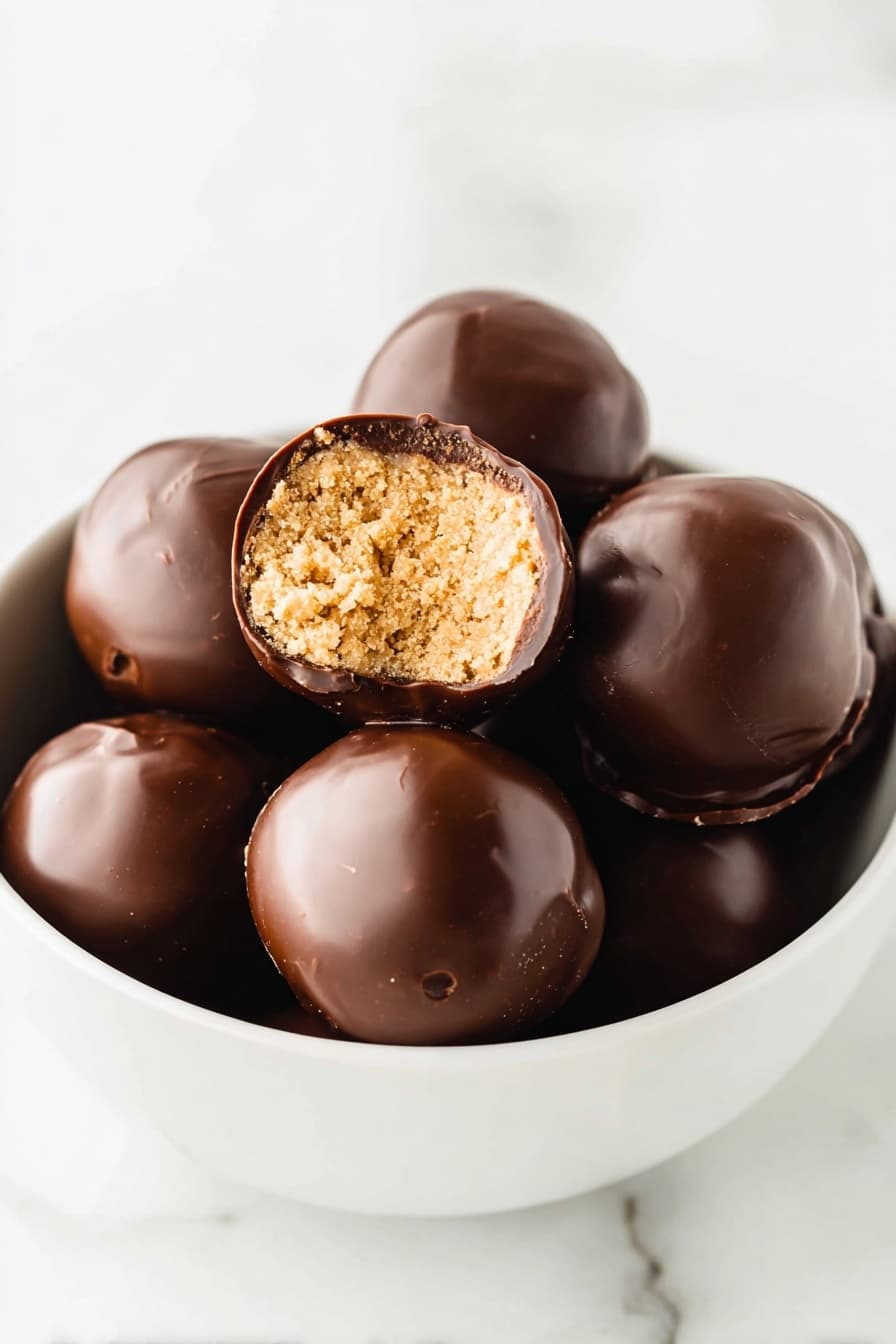 The image shows three round chocolate balls on a white marbled surface, with one ball in the front partially bitten to reveal a thick, light tan peanut butter layer inside. Each ball is coated with a smooth, dark brown chocolate shell and topped with small round sprinkles in red, white, and green, some of which are also scattered on the surface around the balls. The depth of field blurs the two balls in the background, focusing on the bitten one in the front. photo taken with an iphone --ar 2:3 --v 7 - Chocolate Peanut Butter Balls, Peanut Butter Recipes, No-Bake Snacks, Easy Dessert Ideas, Party Treats