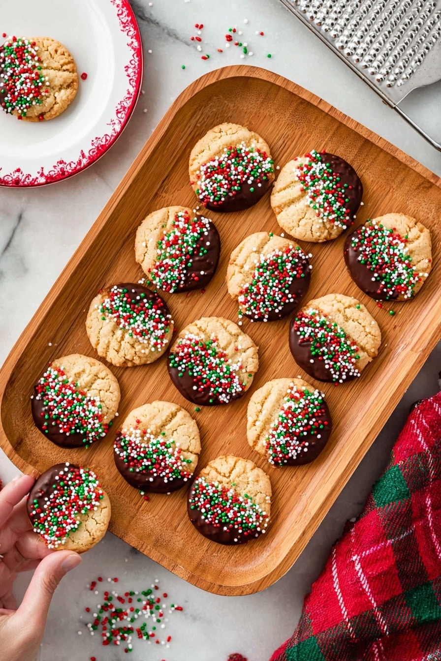 There is a stack of five round cookies on a white plate with a red rim, placed on a white marbled surface. Each cookie is thick and has a cracked light brown texture. The top half of each cookie is dipped in dark chocolate, which looks smooth and shiny. Bright red, green, and white sprinkles cover the chocolate parts, some falling around the plate. The top cookie has a bite missing from its right side, showing the crumbly inside. Photo taken with an iphone --ar 2:3 --v 7 - Peanut Butter Chocolate Christmas Cookies, holiday cookie recipes, easy Christmas cookies, festive cookie ideas, holiday baking treats