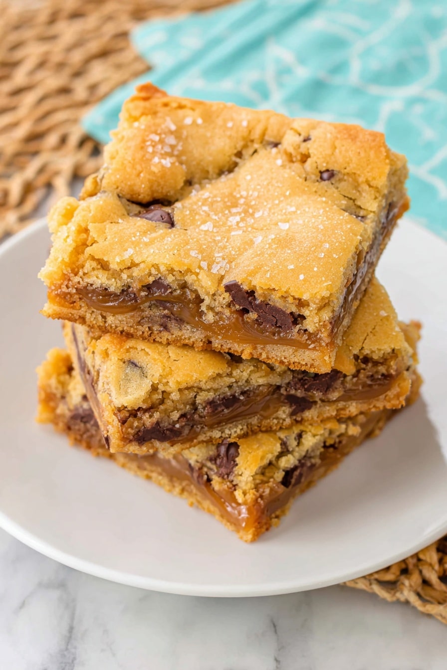 A close-up shows a woman's hand holding a broken square piece of cookie bar with one bite taken off. The cookie bar has two layers: the top layer is light golden brown with a soft, slightly crumbly texture mixed with small dark chocolate chips, and the bottom layer is thicker, darker brown, and dense with melted caramel oozing where the piece broke. In the background, more cookie bars are stacked on a white plate on a white marbled surface, with a blurred glass of milk nearby. The scene is brightly lit with natural light. photo taken with an iphone --ar 2:3 --v 7 - Salted Caramel Chocolate Chip Cookie Bars, caramel cookie bar recipe, easy caramel cookie bars, gooey caramel cookie bars, homemade caramel cookie bars