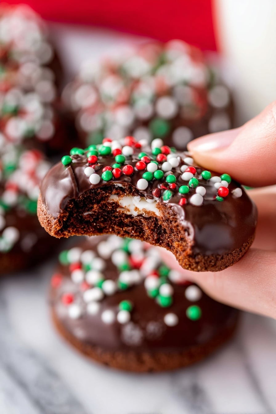 Round chocolate cookies are laid out on a metal cooling rack over a white marbled surface. Each cookie has two layers: the base is a dense, brown cookie with a rough texture, and the top is a thick, shiny, dark chocolate layer spread unevenly with a rounded chocolate piece in the middle. Sprinkles in red, green, and white colors are scattered on the chocolate topping, giving a festive look. The cookies are arranged closely together in rows, filling the frame. photo taken with an iphone --ar 2:3 --v 7 - Hot Chocolate Cookies with Marshmallows, chocolate cookies with marshmallows, cozy chocolate treat, easy hot chocolate cookies, gooey marshmallow cookies