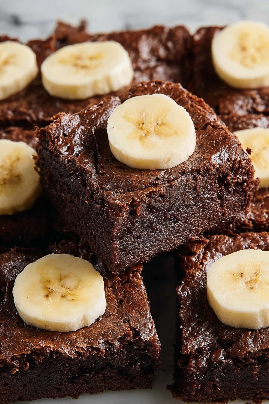 A stack of three thick, dark brown chocolate brownies with a moist and slightly crumbly texture sits on a white marbled surface; the bottom brownie shows chunks of chocolate embedded inside it, the middle brownie is rich and dense with some melting chocolate on top, and the top brownie has two thick slices of pale yellow banana resting on it, adding a soft contrast in color and texture. photo taken with an iphone --ar 2:3 --v 7 - Banana Chocolate Brownies, chocolate banana brownies, fudgy banana brownies, easy banana brownies, moist chocolate brownies