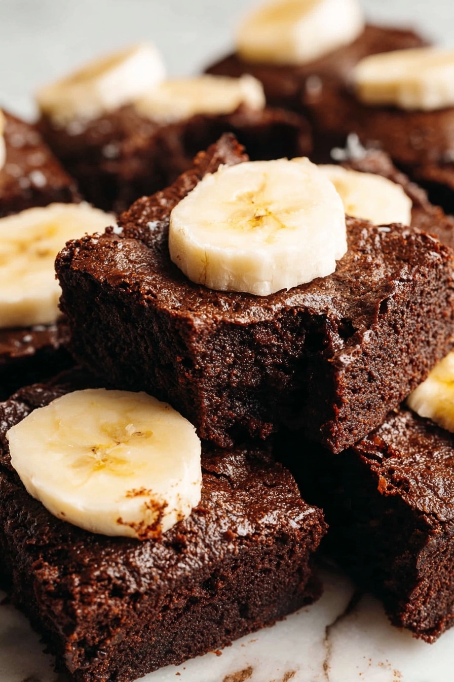The image shows a close-up view of several square pieces of rich dark brown chocolate brownies stacked on a white marbled surface. Each brownie has a textured, slightly shiny top layer with a dense and moist interior visible on some edges. On top of most brownie pieces, there are two to three thick slices of pale yellow banana arranged flat, adding a fresh contrast to the dark brownies. The brownies fill the frame with parts overlapping, and the focus is sharp on the front pieces with a soft blur on the ones in the back. photo taken with an iphone --ar 2:3 --v 7 - Banana Chocolate Brownies, chocolate banana brownies, fudgy banana brownies, easy banana brownies, moist chocolate brownies