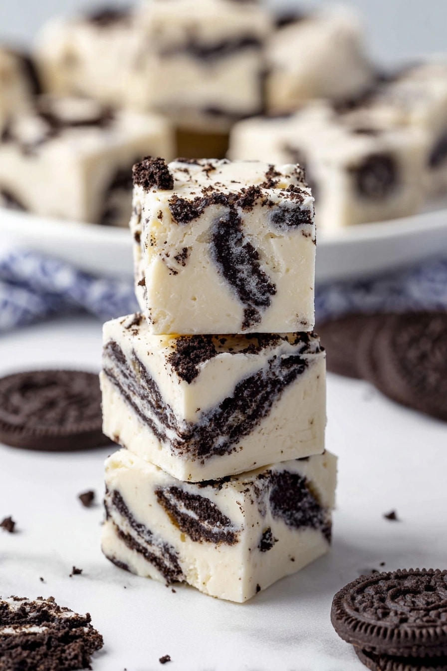 The image shows a white plate filled with square pieces of layered dessert. Each piece has three visible layers of dark brown cookie bits separated by creamy white layers of frosting or cream. The creamy layers cover the top and sides of each square, with some cookie crumbs scattered on top. In the background, there are stacks of whole dark brown cookies blurred out, all placed on a surface with white marbled texture. photo taken with an iphone --ar 2:3 --v 7 - Easy Oreo Fudge, Oreo Fudge, no-bake Oreo dessert, simple fudge recipe, quick Oreo treats