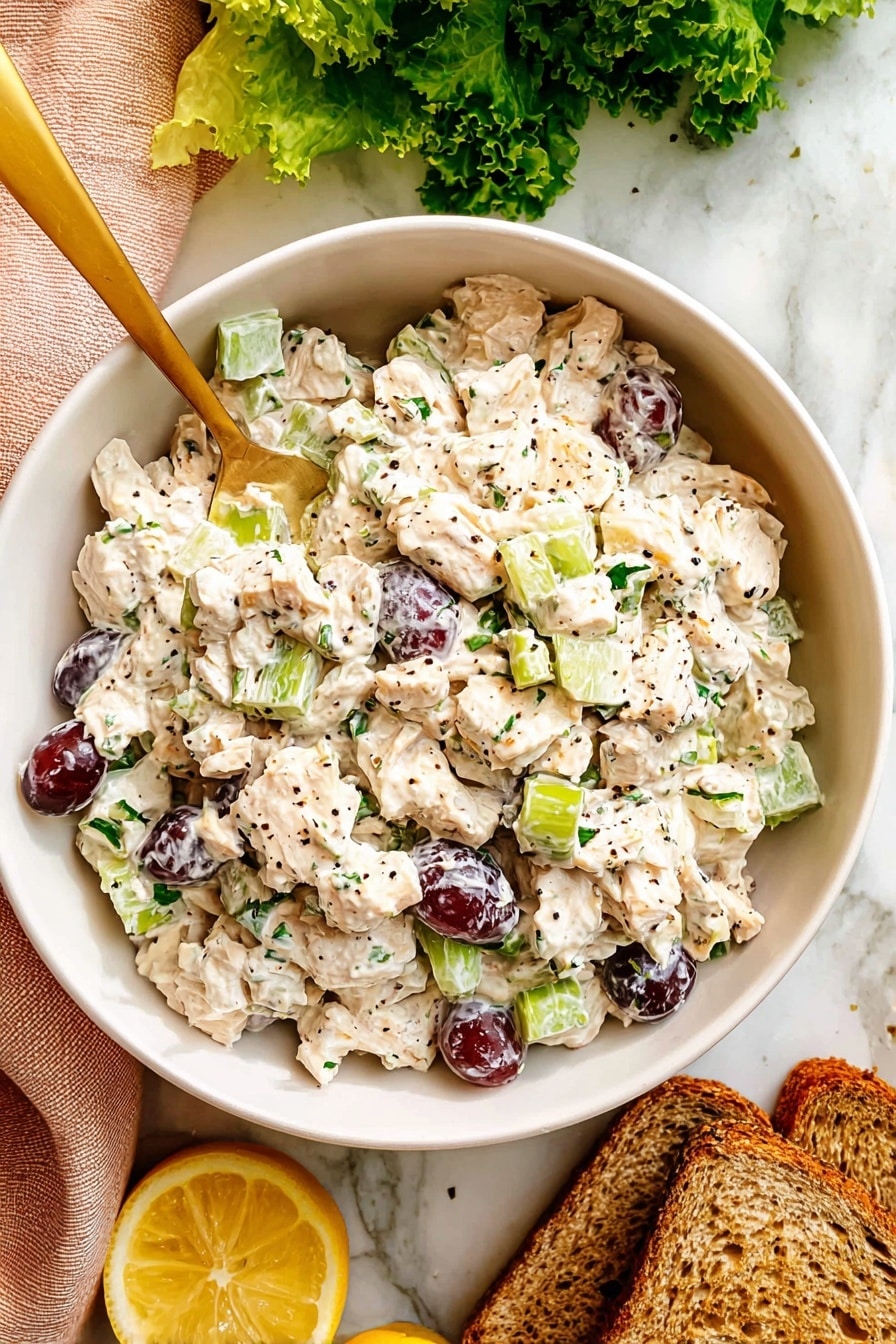 Two sandwich halves are stacked, each with three layers: the top and bottom are light brown whole wheat bread with a slightly rough texture. Inside the sandwich, there are bright green leafy lettuce layers that curl around the filling. The filling is creamy white with visible pieces of light green celery and small chunks of pale chicken mixed with mayonnaise. Some dark red grape halves are peeking from the sides. The sandwich is held together with a wooden toothpick and placed on a white plate over a white marbled surface. Photo taken with an iphone --ar 2:3 --v 7 - Healthy Chicken Salad with Grapes and Almonds, light chicken salad, nutritious fruit and nut salad, easy healthy chicken salad, fresh grape chicken salad