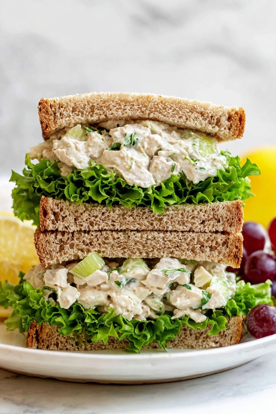 A white bowl filled with a creamy chicken salad that has three main layers: white creamy dressing mixed with beige chicken pieces, bright green celery and green onions, and dark red grapes scattered throughout. The salad has a slightly chunky texture, sprinkled with black pepper on top. A gold spoon is placed inside the bowl. Around the bowl, there are two squeezed lemon halves with a bright yellow peel, some fresh green lettuce leaves in the upper background, and two slices of toasted brown bread on the right side, all set on a white marbled surface with a light peach cloth partially visible on the left. Photo taken with an iphone --ar 2:3 --v 7 - Healthy Chicken Salad with Grapes and Almonds, light chicken salad, nutritious fruit and nut salad, easy healthy chicken salad, fresh grape chicken salad